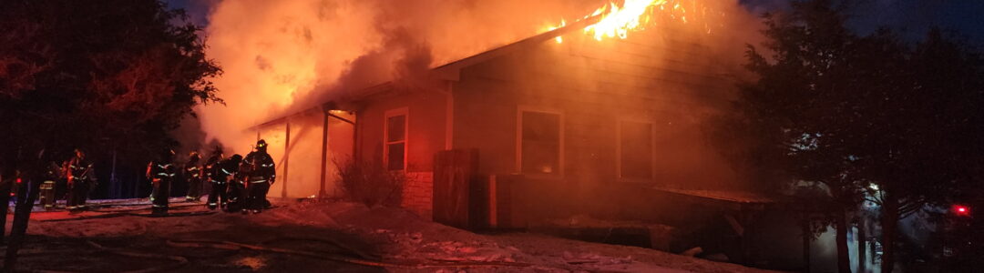 House on fire at night with firefighters spraying water.